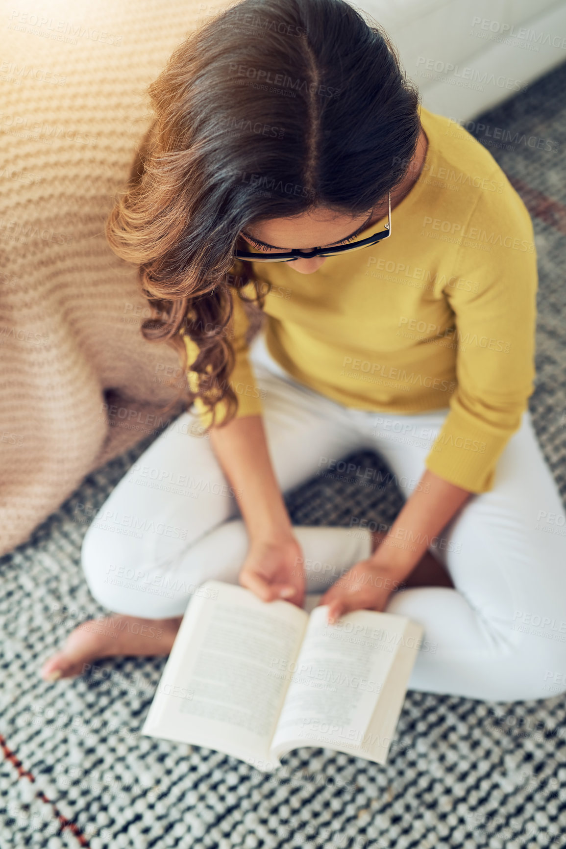 Buy stock photo Shot of a young woman reading a book while relaxing at home