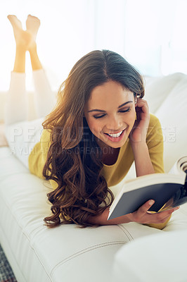 Buy stock photo Shot of a young woman reading a book while relaxing at home