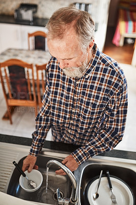 Buy stock photo Shot of a focused senior man washing dishes in the kitchen at home