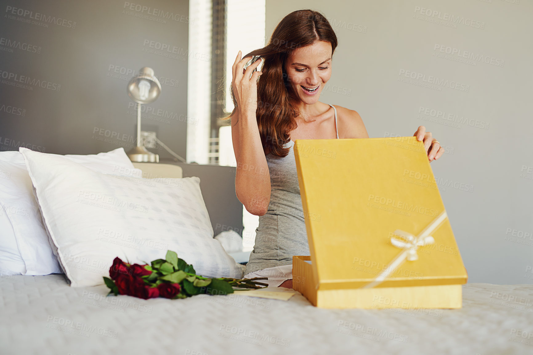 Buy stock photo Shot of a young woman opening a surprise gift at home