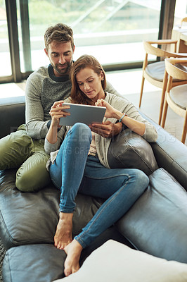 Buy stock photo High angle shot of an affectionate young couple using a tablet while relaxing on their sofa at home