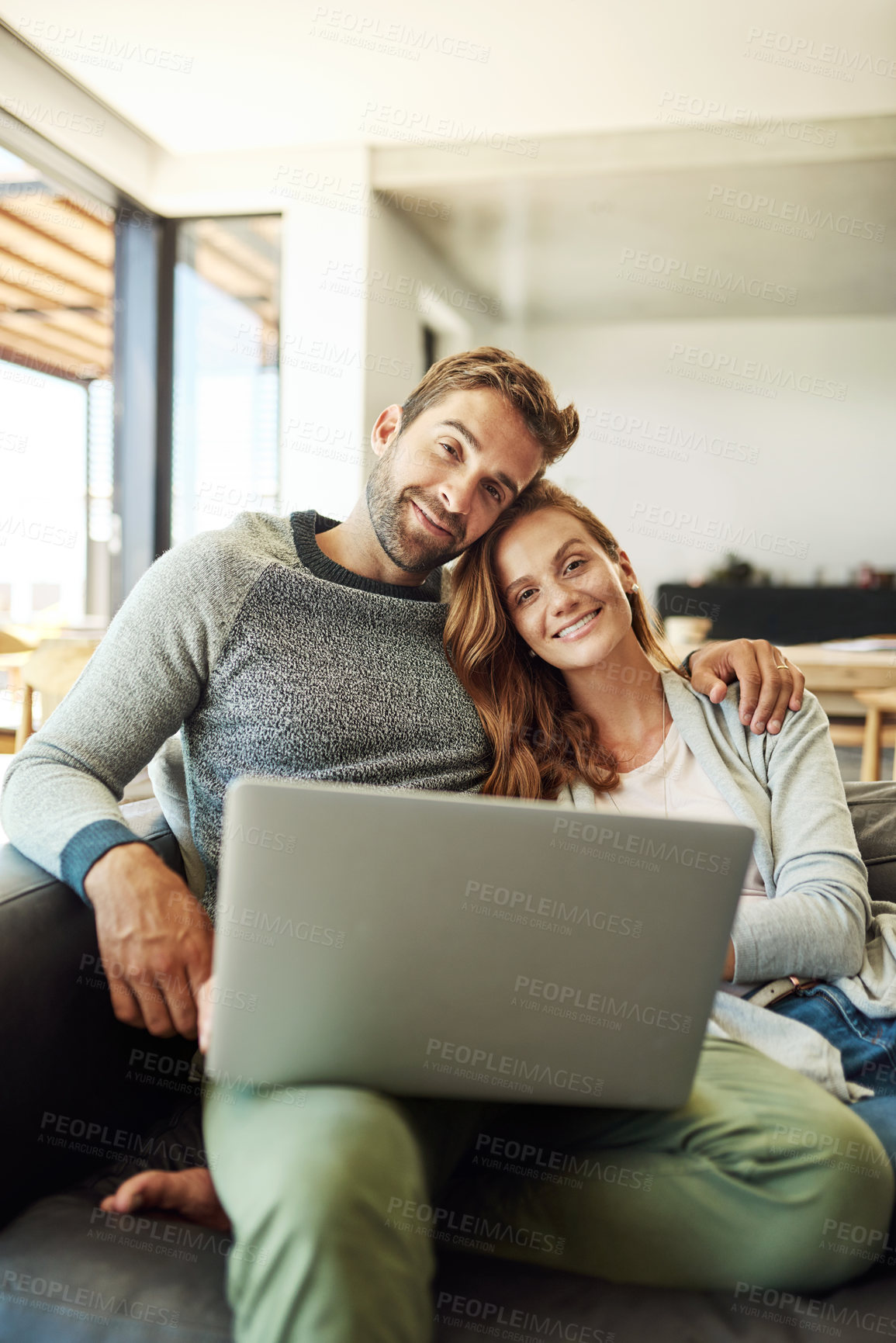 Buy stock photo Cropped portrait of an affectionate young couple using a laptop while relaxing on their sofa at home