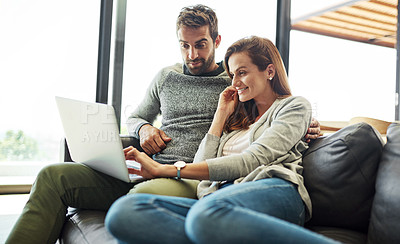 Buy stock photo Low angle shot of an affectionate young couple using a laptop while relaxing on their sofa at home
