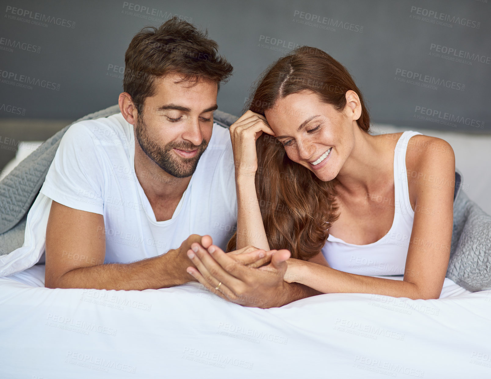 Buy stock photo Happy couple, relax or holding hands on bed in morning, peace or love for marriage commitment at house. Palm reading, together or people with smile for romantic relationship, bonding or anniversary