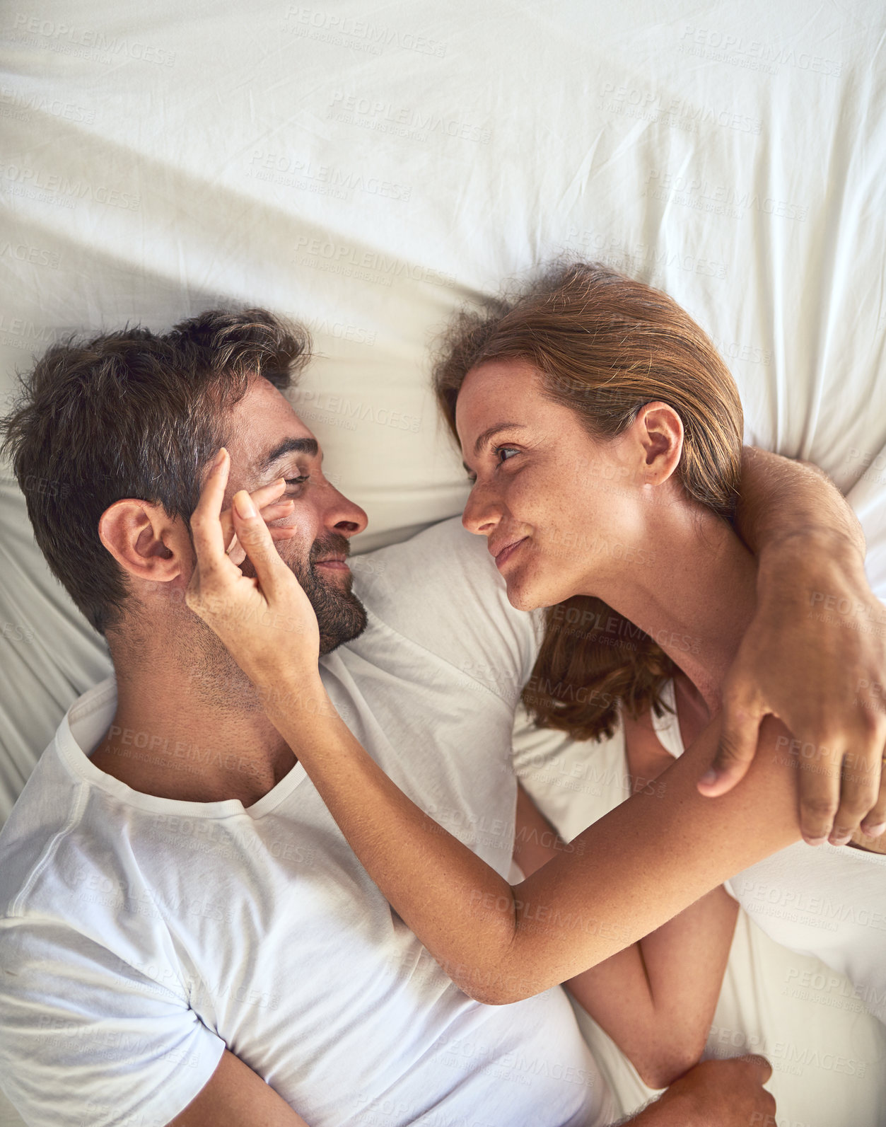 Buy stock photo Love, couple and smile to relax on bed above view for bonding, peace or support of marriage commitment at house. Woman, man and touching face for embrace, care or relationship romance on anniversary