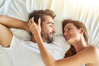 Buy stock photo High angle shot of a happy young couple relaxing in bed together at home