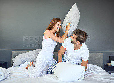 Buy stock photo Shot of a happy young couple having a pillow fight in bed
