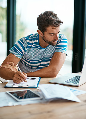 Buy stock photo Cropped shot of a handsome young male entrepreneur making notes while working from his home office