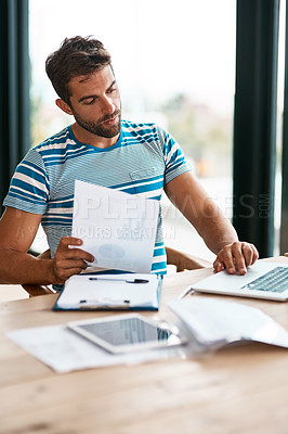 Buy stock photo Cropped shot of a handsome young male entrepreneur going over some paperwork while working from his home office