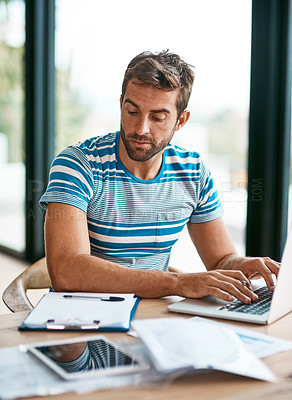Buy stock photo Cropped shot of a handsome young male entrepreneur going over some paperwork while working from his home office