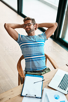 Buy stock photo High angle shot of a handsome young male entrepreneur sitting with his hands behind his head while working from his home office