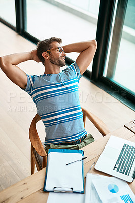 Buy stock photo High angle shot of a handsome young male entrepreneur sitting with his hands behind his head while working from his home office