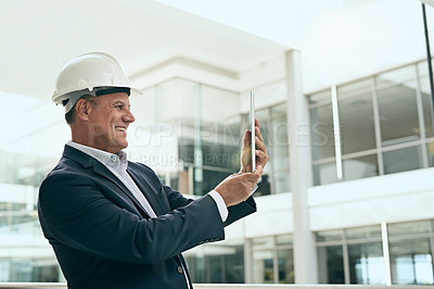Buy stock photo Shot of a cheerful professional male architect taking a photo of a development site with his digital tablet inside a building