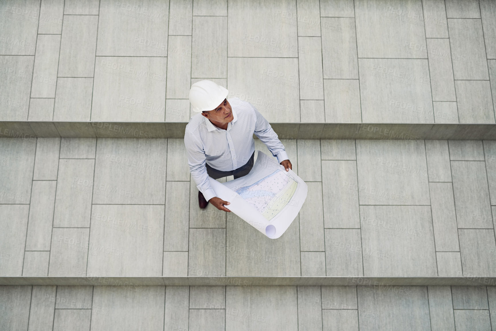 Buy stock photo High angle shot of a focused professional male architect holding blueprints while looking up inside of a building