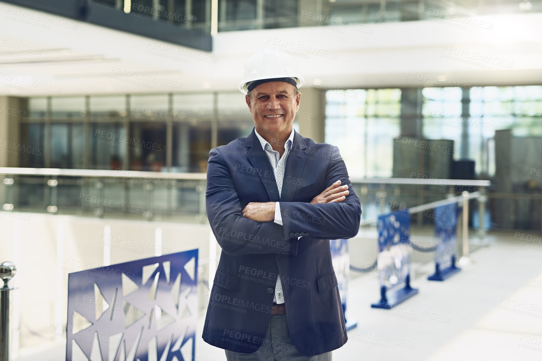 Buy stock photo Portrait of a cheerful professional male architect standing with arms folded while looking at the camera inside of a building