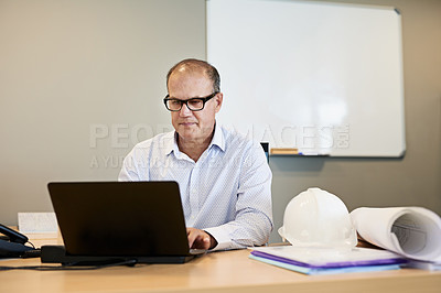 Buy stock photo Shot of a focused professional businessman working on his laptop while being seated in a office