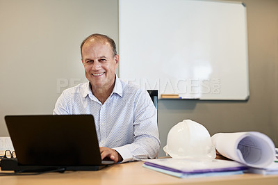 Buy stock photo Portrait of a cheerful professional businessman working on his laptop while looking at the camera inside the office