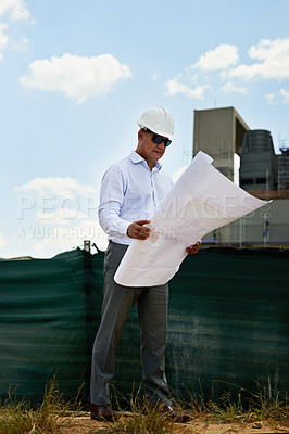 Buy stock photo Shot of a professional male architect standing on a building site while holding and reading blueprints outside