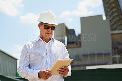 Buy stock photo Shot of a professional male architect on a building site while working on a digital tablet outside