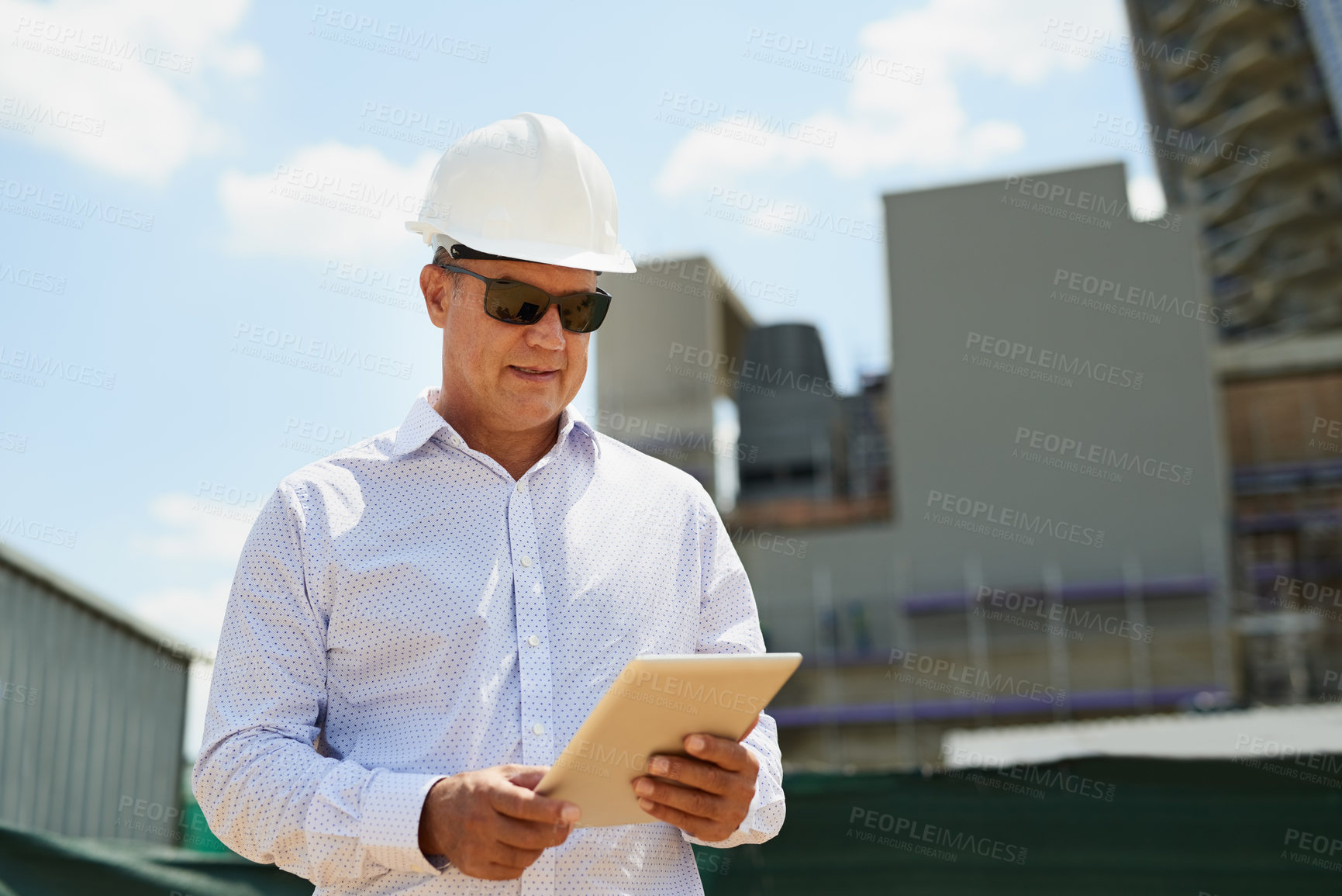 Buy stock photo Shot of a professional male architect on a building site while working on a digital tablet outside