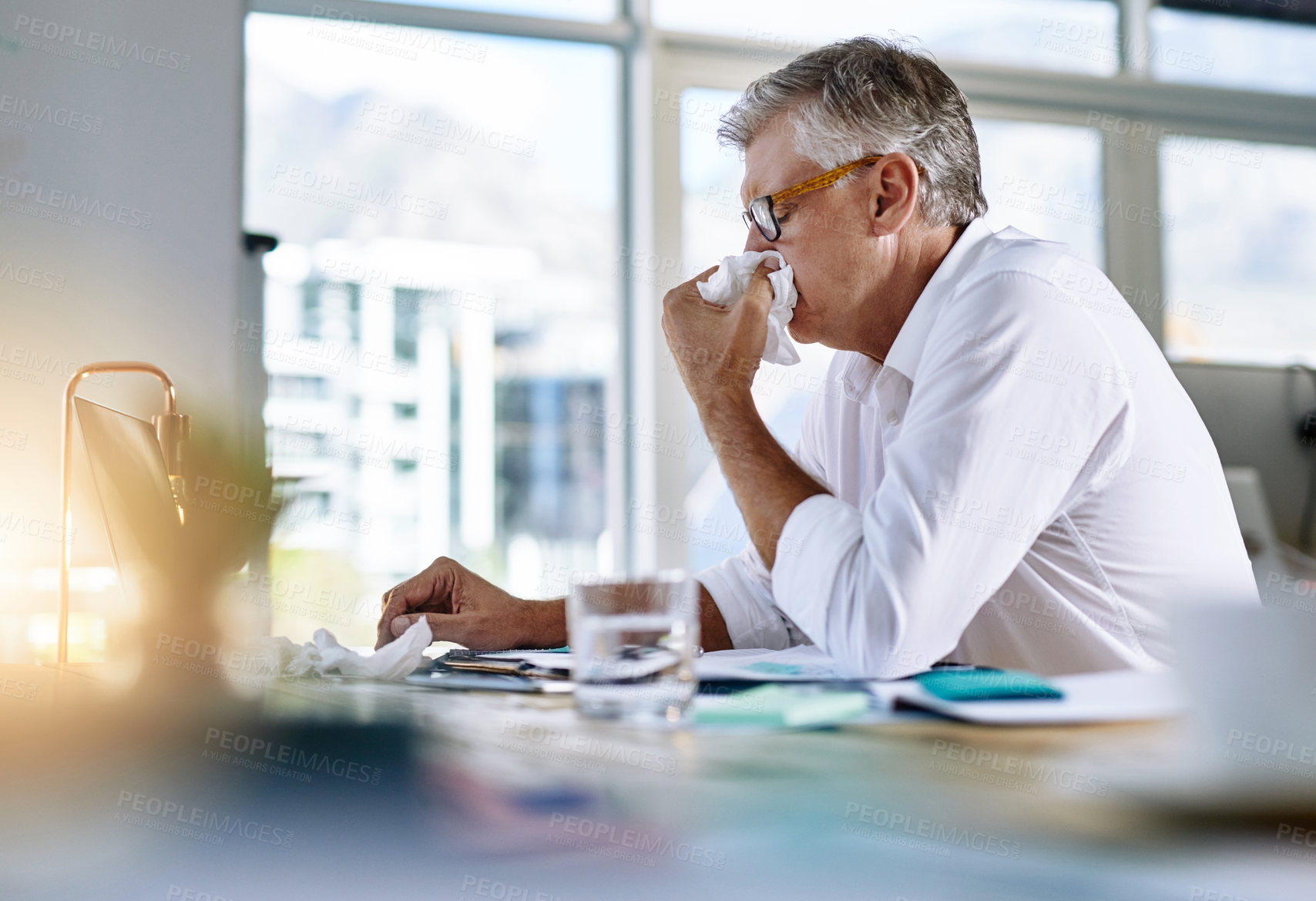 Buy stock photo Shot of a mature businessman blowing his nose in the office