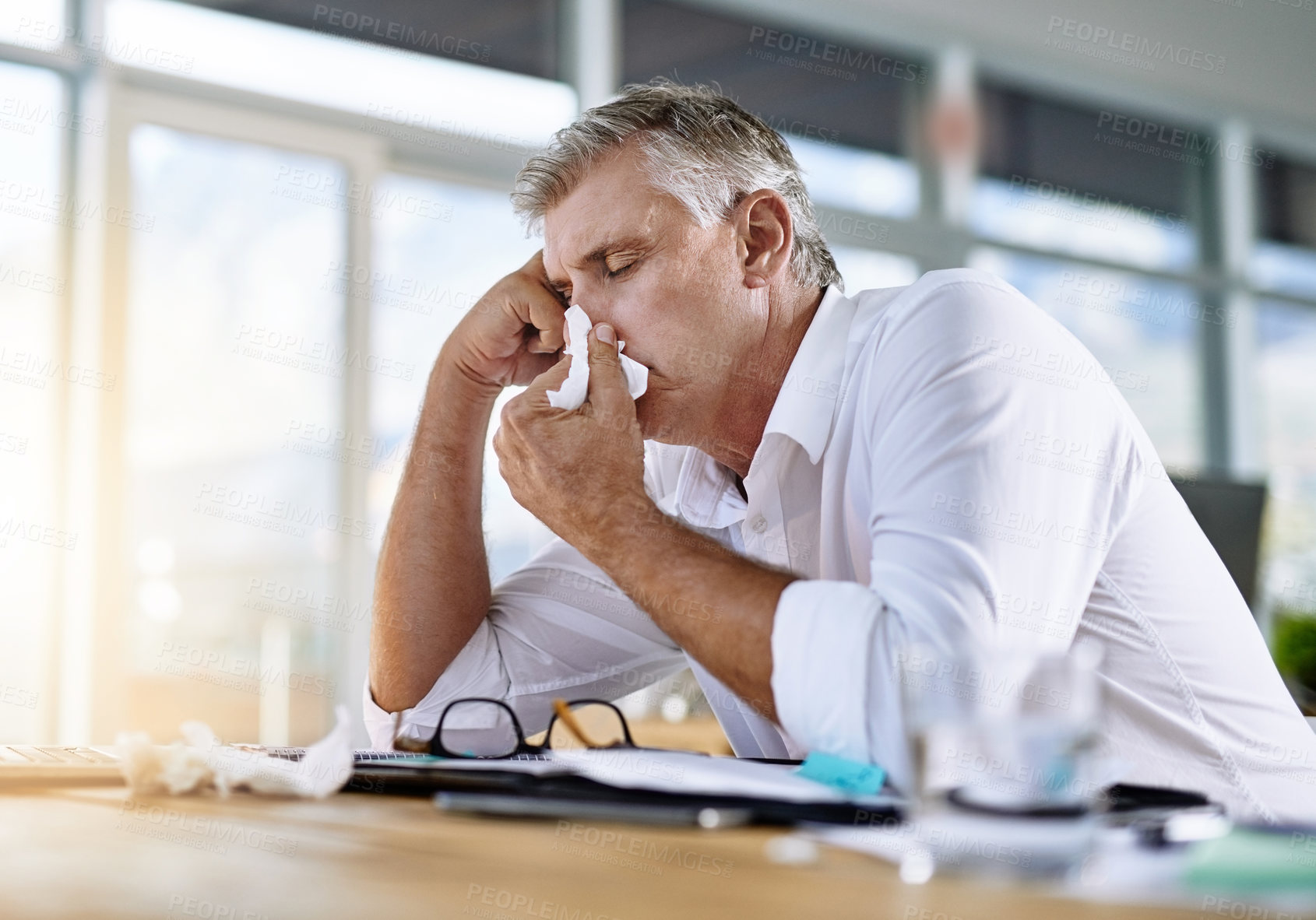 Buy stock photo Mature, businessman and blowing nose with tissue at office for flu, cold or viral infection on desk. Sick, man or frustrated employee with virus, sneeze or allergy for sinus or symptoms at workplace