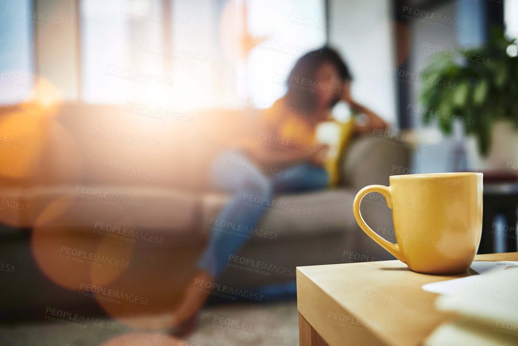 Buy stock photo Closeup shot of a mug on a coffee table with an unrecognizable young woman relaxing in the background