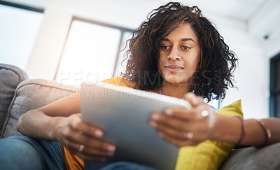 Buy stock photo Low angle shot of an attractive young woman using her tablet while relaxing at home on the weekend