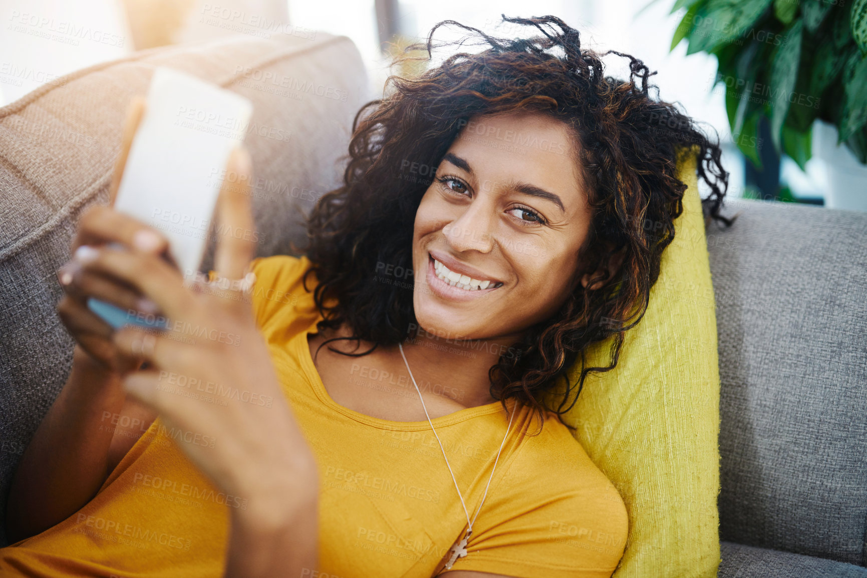 Buy stock photo High angle portrait of an attractive young woman using her cellphone while relaxing at home on the weekend