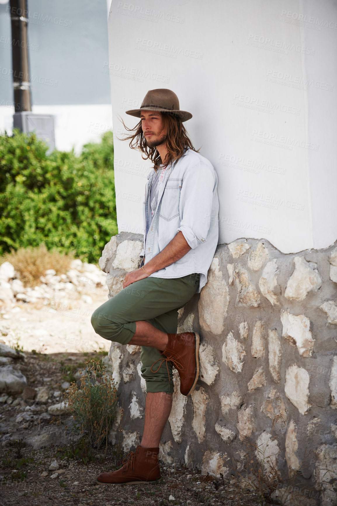 Buy stock photo Shot of a trendy young man leaning against the wall of a building outside