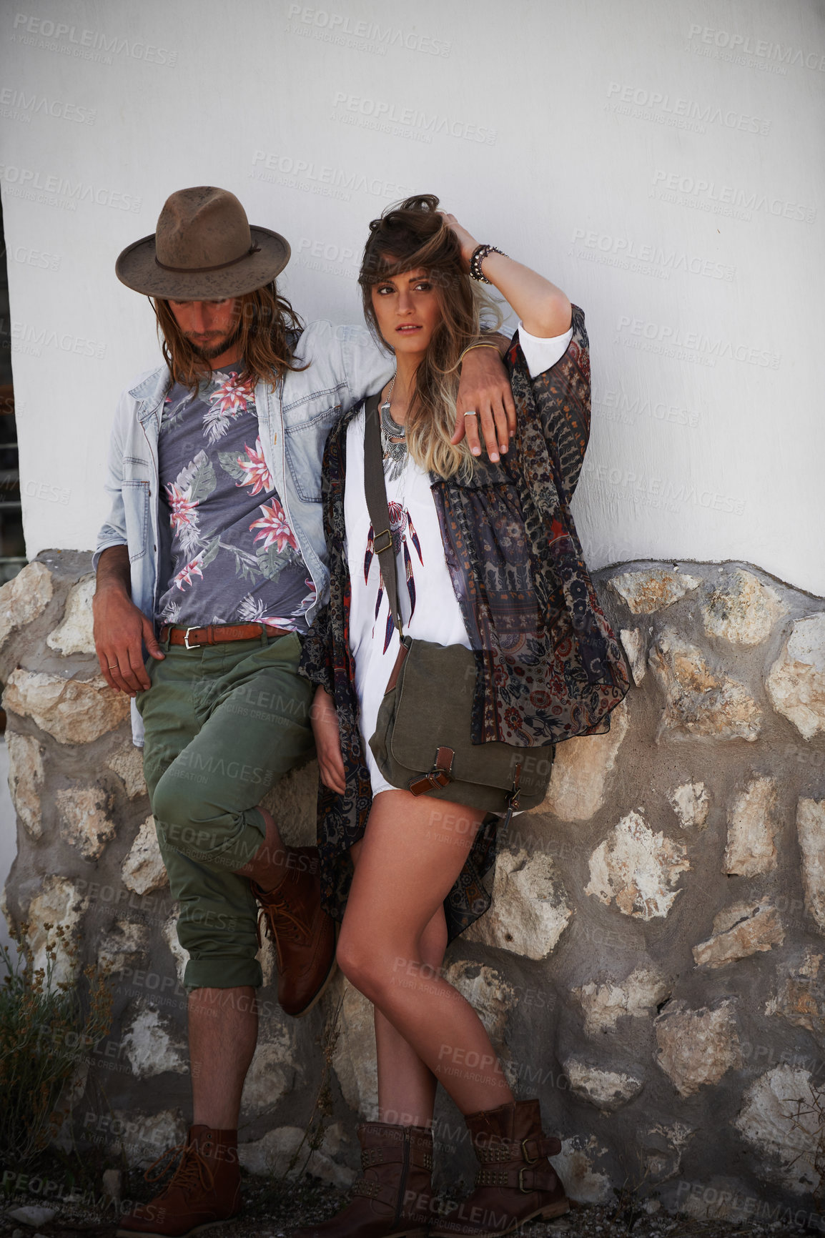 Buy stock photo Shot of a trendy young couple standing together against the wall of a building outside