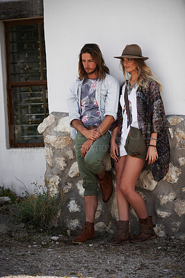 Buy stock photo Shot of a trendy young couple standing together against the wall of a building outside