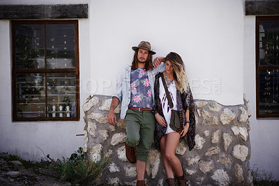 Buy stock photo Shot of a trendy young couple standing together against the wall of a building outside