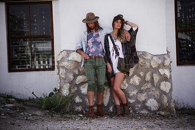 Buy stock photo Shot of a trendy young couple standing together against the wall of a building outside