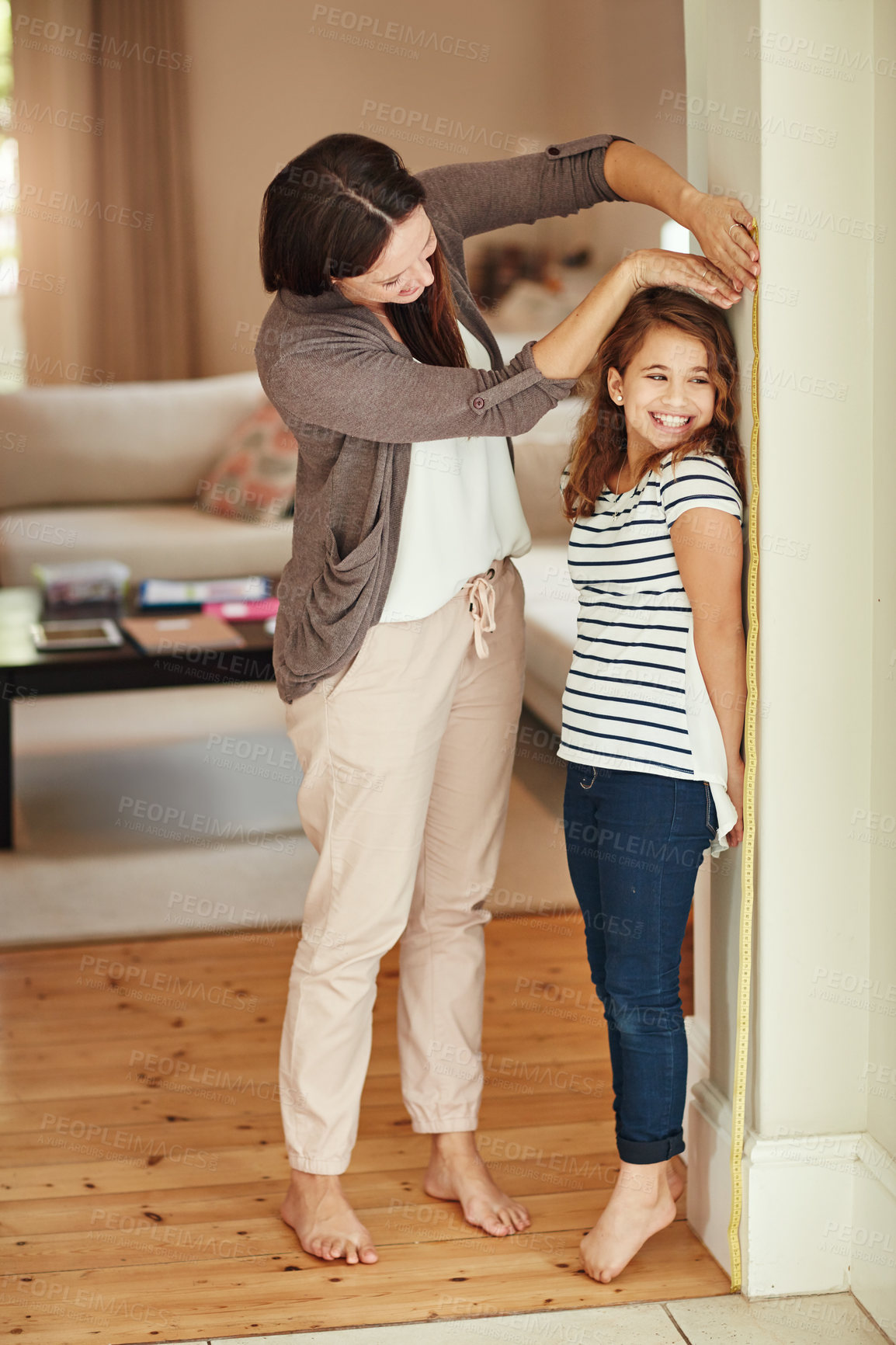 Buy stock photo Shot of a beautiful mother measuring her adorable daughter's height at home