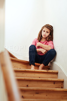 Buy stock photo Shot of a little girl looking sad while sitting on the stairs at home