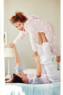 Buy stock photo Shot of a young mother lifting her daughter with her legs while lying on bed