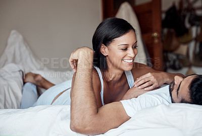 Buy stock photo Shot of an affectionate young couple lying on a bed together at home