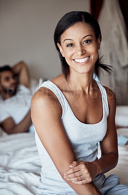 Buy stock photo Portrait of a young woman sitting on a bed with her husband in the background at home