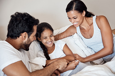 Buy stock photo Shot of parents tickling their little daughter while lying in bed together at home