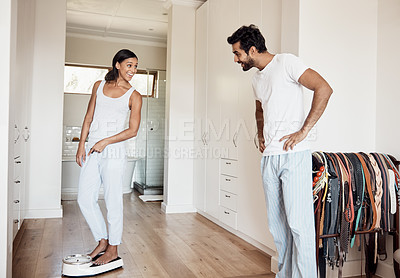 Buy stock photo Shot of a woman weighing herself on a scale while her husband watches at home