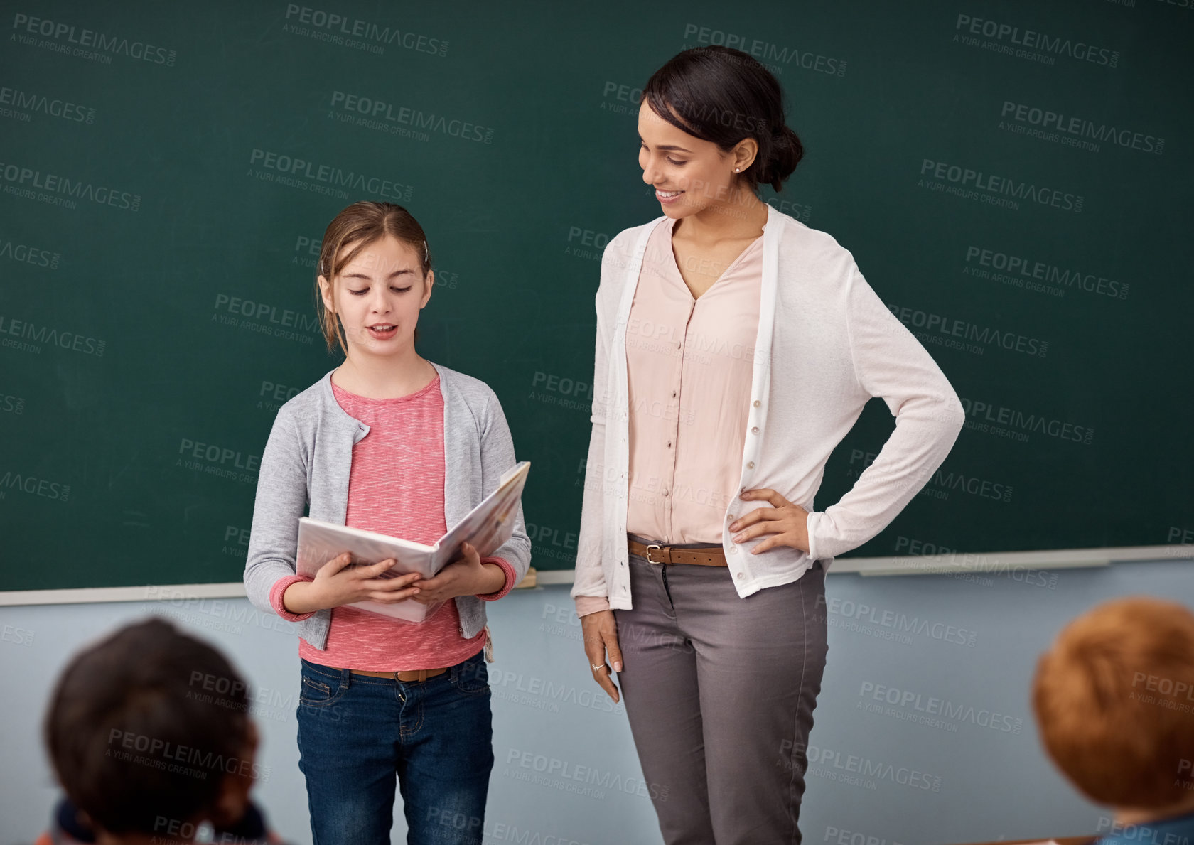 Buy stock photo Shot of an elementary school girl reading in front of the class while standing alongside her teacher