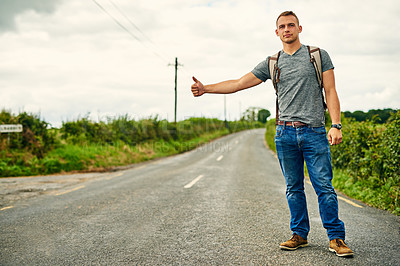 Buy stock photo Shot of a young man hitchhiking on the roadside