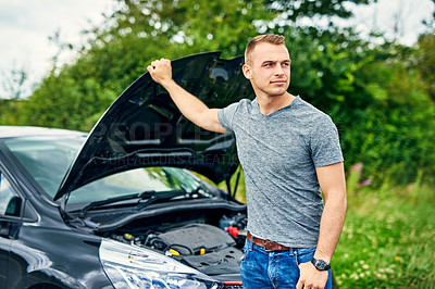 Buy stock photo Shot of a young man checking under the hood of his car after breaking down on the road