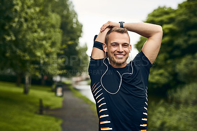 Buy stock photo Portrait of a sporty young man stretching before a run outdoors
