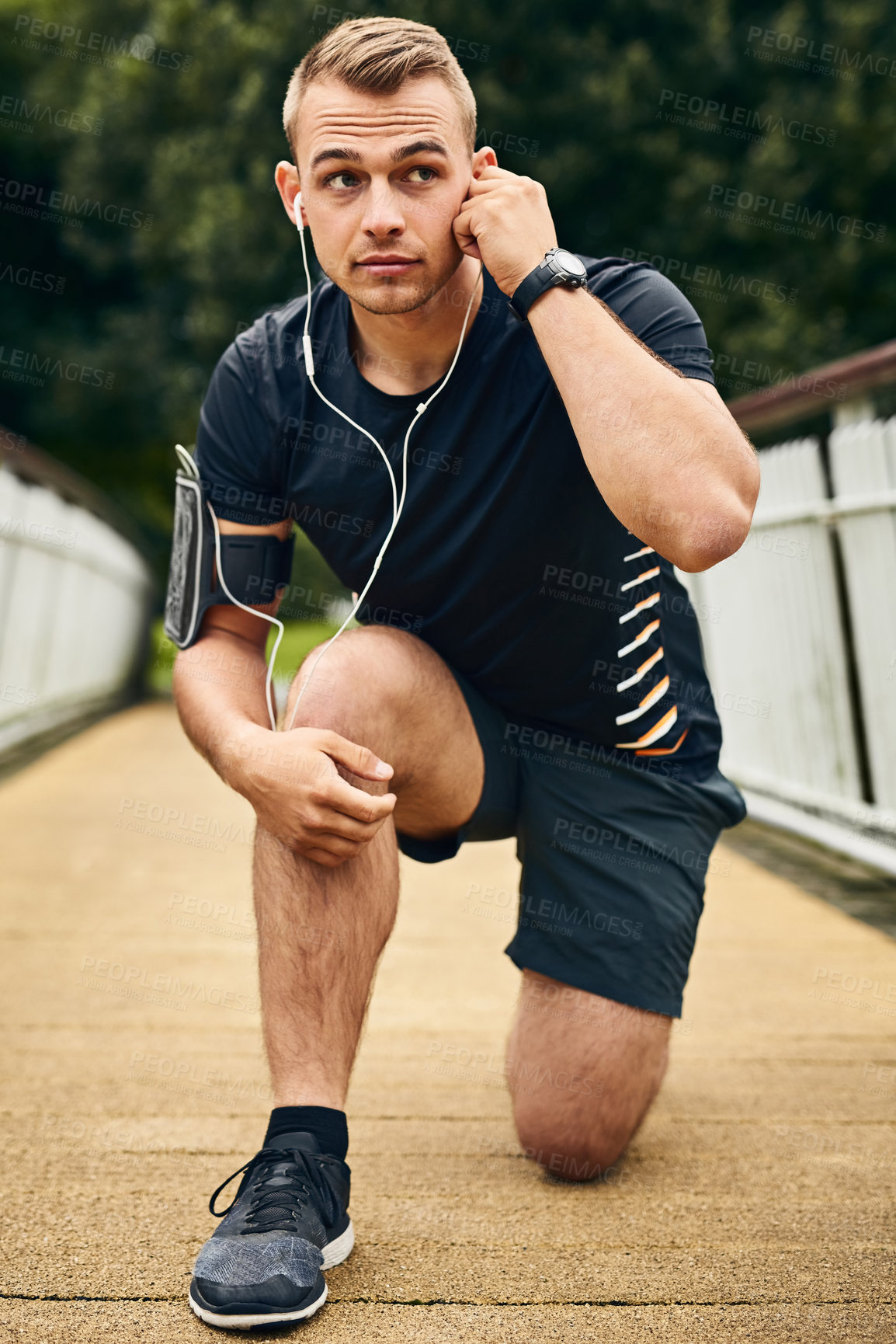 Buy stock photo Shot of a sporty young man tying his shoelaces while exercising outdoors