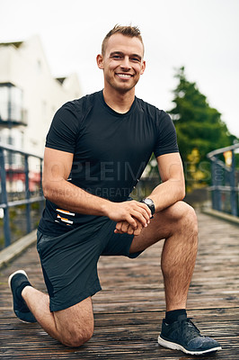 Buy stock photo Portrait of a sporty young man tying his shoelaces while exercising outdoors