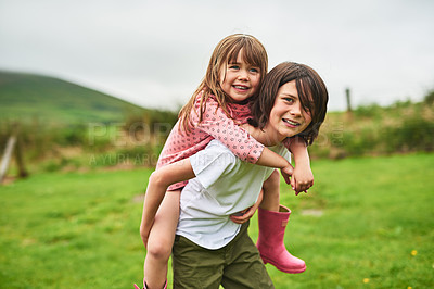 Buy stock photo Portrait of a little boy giving his sister a piggyback ride outdoors