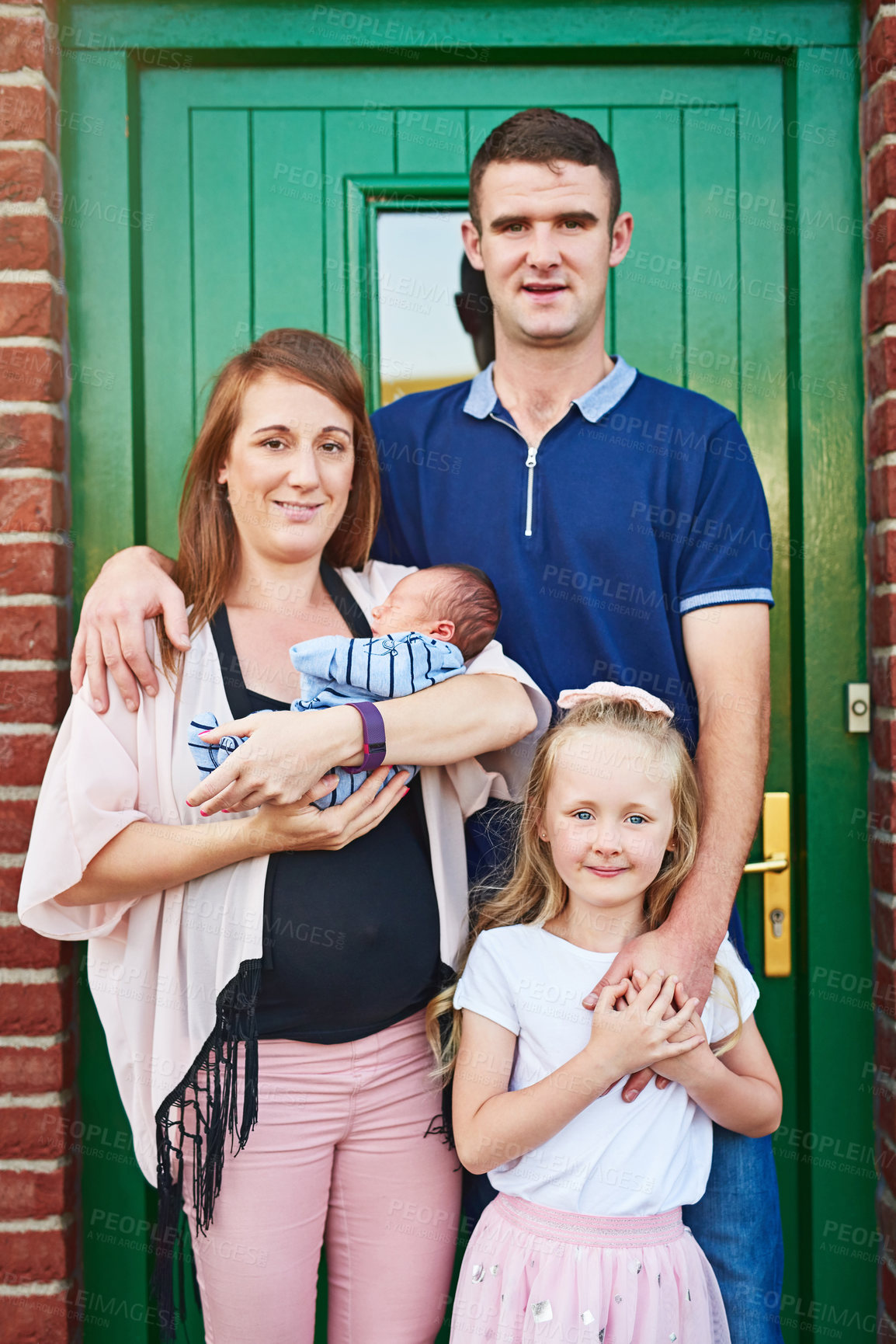 Buy stock photo Portrait of a cheerful young family grouped together while looking at the camera outside