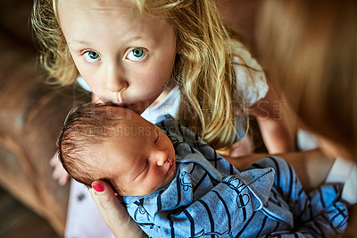 Buy stock photo Shot of a cheerfull affectionate little girl giving her little baby brother a kiss in the forehead while looking at the camera at home